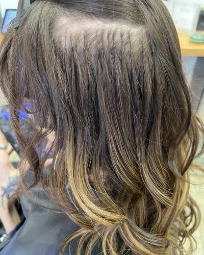 Close-up of a row of small keratin bonds at the part, with the extension hair blended into curled ends